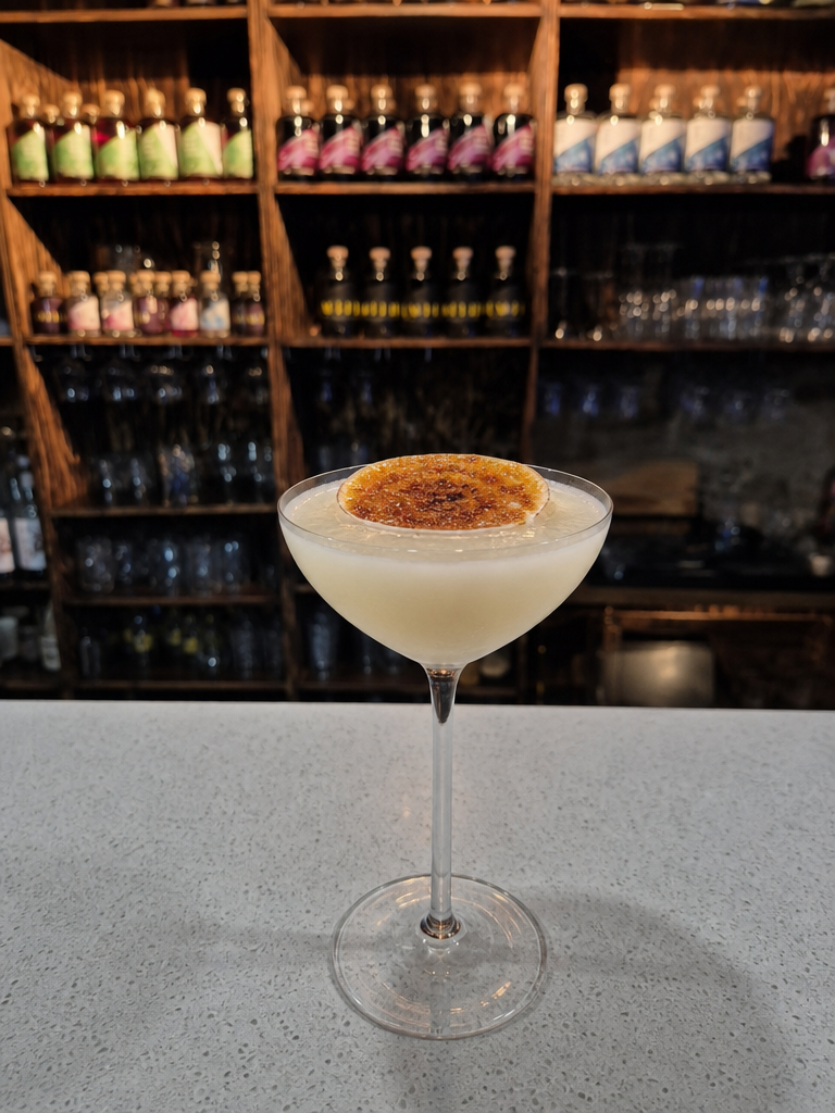 A Creme de Gin cocktail in a coupe glass with a brûléed lemon wheel on top